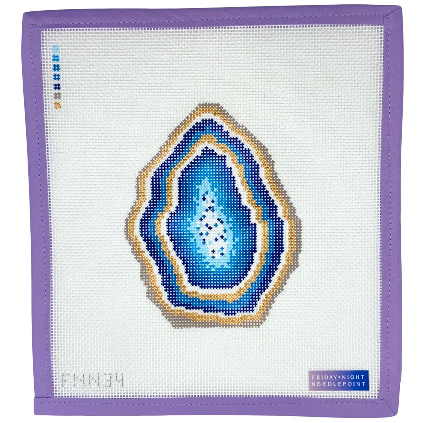 Needlepoint canvas with a blue and gold geode design on a white fabric background, framed by a purple border.